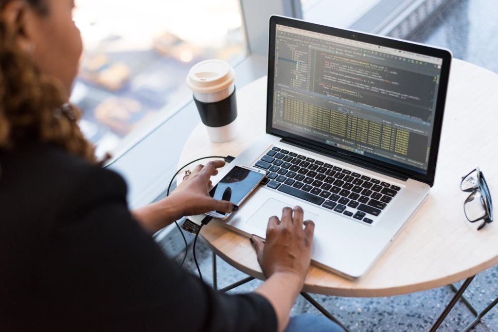 black-and-silver-laptop-computer-on-round-brown-wooden-table-1181243 Black woman programming on a laptop with coffee, smartphone, and glasses on a desk in an office.